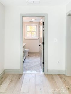 an empty room with white walls and wood flooring is seen from the doorway to the kitchen