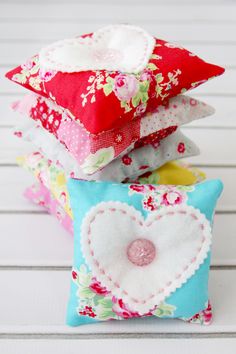 four pillows stacked on top of each other in different colors and patterns, one with a heart