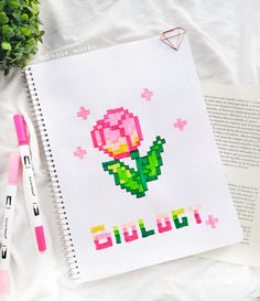 a cross stitch book with a pink rose on it next to a marker and pen