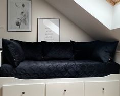 a bed with black sheets and pillows under a slanted ceiling