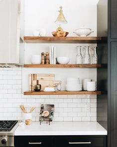 a kitchen with black cabinets and white subway backsplash, gold accents on the shelves