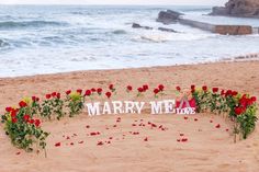 there is a sign that says marry me on the beach with roses around it and flowers in the sand