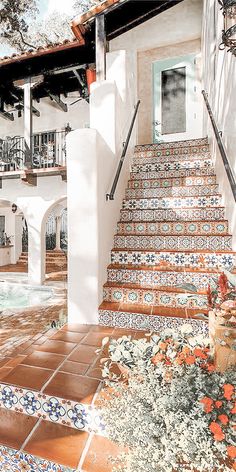 an outdoor swimming pool next to a white house with colorful tiles on the steps leading up to it