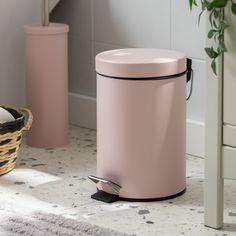 a pink trash can sitting on the floor next to a basket and potted plant