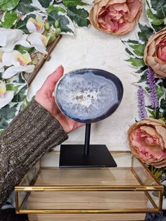 a person holding up a blue object in front of some pink flowers and greenery