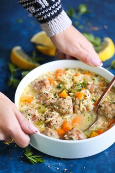 two hands holding a bowl of soup with meat and veggies on the side