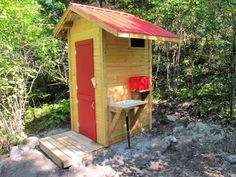 a small outhouse in the woods with a red roof and door on it's side