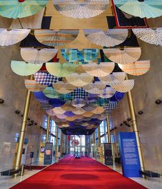 several umbrellas hanging from the ceiling in a large room with red carpet and white walls