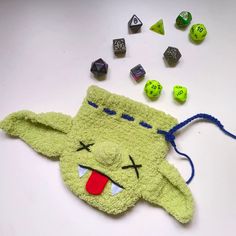 a green stuffed animal laying on top of a table next to dices and beads