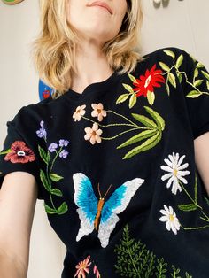 a woman wearing a black shirt with colorful flowers on it and a butterfly embroidered on the back