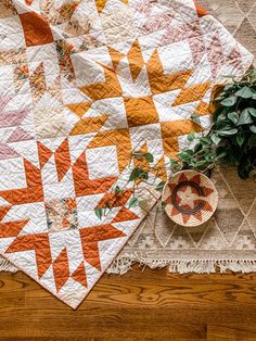 an orange and white quilt sitting on top of a wooden floor next to a potted plant