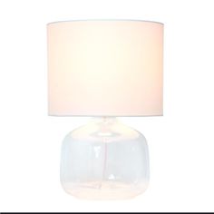 a clear glass lamp with a white shade on the base and a light bulb attached to it