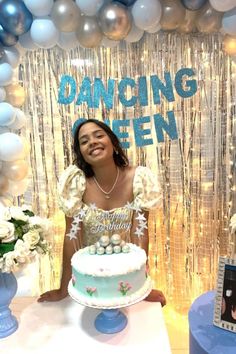 a woman sitting in front of a cake on top of a table next to balloons