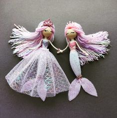 two little mermaid dolls sitting next to each other on top of a black surface,