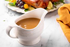 a white gravy pitcher sitting on top of a table next to a plate of food