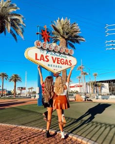 two women standing in front of the welcome to las vegas sign with their hands up