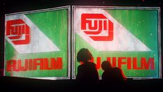 two people standing in front of a large screen with the words fuji film on it