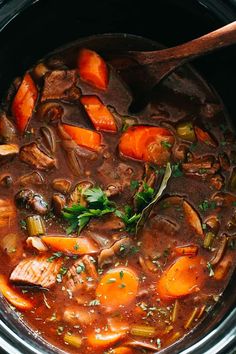 a stew with carrots, mushrooms and meat in a crock pot on the stove