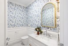 a bathroom with blue and white wallpaper, gold framed mirror, toilet and sink