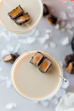 two glasses filled with desserts on top of a white table next to flowers and ice