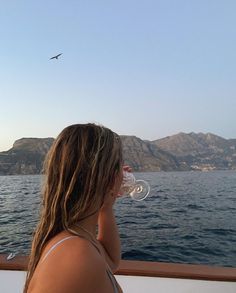 a woman drinking wine from a glass while sitting on the back of a boat in the ocean