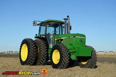 a green tractor is parked in the middle of a field with yellow rims on it's tires