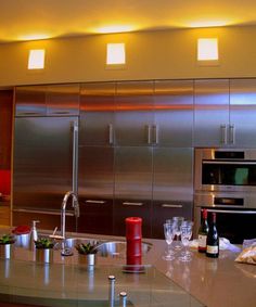 a modern kitchen with stainless steel appliances and counter tops, along with wine glasses on the bar