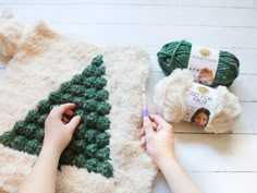 someone is crocheting a christmas tree on the floor next to two balls of yarn