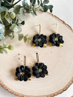 This listing is for one pair of black flower dangle earrings. Each flower is sculpted from black polymer clay. The petals were individually cut out and shaped into a flower shape with a textured heart on the back of the earring. Brass leaves were placed between the layers of petals and gold glitter was added to the flower centers. Please be advised that some glitter may fall off. Each earring was cured in the oven and the stud portion is nickel-free.  Care: Please treat your new earrings as litt Black Flower Charm Jewelry, Black Flower Earrings For Gift, Black Polymer Clay Earrings With Ear Wire, Handmade Black Drop Flower Earrings, Handmade Adjustable Black Flower Earrings, Black Dangle Flower Earrings With Ear Wire, Handmade Black Drop Earrings, Adjustable Black Jewelry With Flower Charm, Handmade Black Polymer Clay Earrings