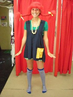 a woman with red hair and blue dress standing in front of a red curtain wearing a clown wig