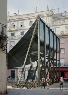 people walking around in front of a building with a large structure on it's side