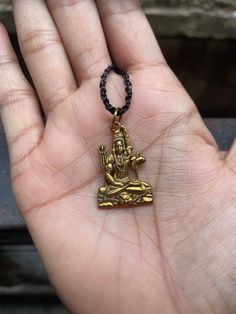 a hand holding a small gold buddha charm