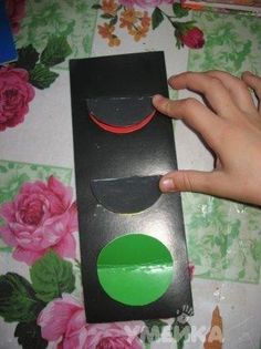 a hand is pointing at a black box with a green circle in it on a floral tablecloth