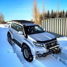 an suv is parked in the snow near a fence