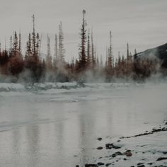 steam rising from the water in front of trees and snow covered ground with rocks on both sides