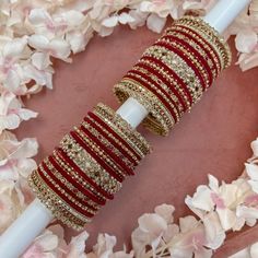 a stack of red and gold bracelets sitting on top of a white pole next to flowers