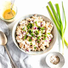 a bowl filled with chicken salad next to two spoons and a glass of orange juice