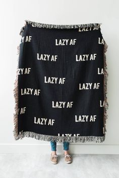 a woman is holding up a black blanket with the word lazy af on it in white letters