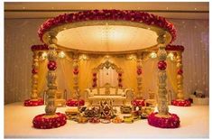 a decorated stage with red and gold flowers on the floor, surrounded by white linens