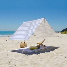 a white and blue sail on the beach with two straw bags under it next to an umbrella