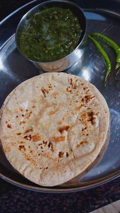 a plate with some food on it next to a small bowl and green chilies