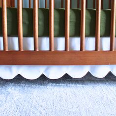 a baby crib with white ruffles on the bottom and green bedding