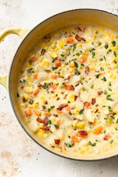 a pot filled with corn and cheese on top of a white countertop next to a wooden spoon