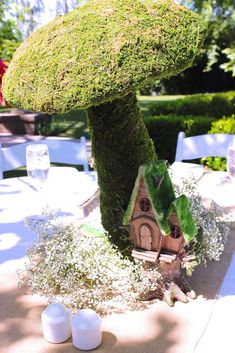 a table topped with a moss covered mushroom next to a small house on top of a tree