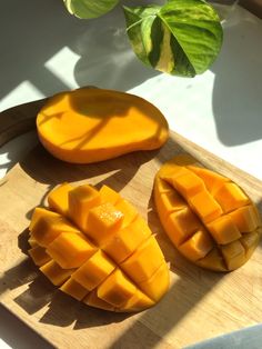 two pieces of mango sitting on top of a wooden cutting board next to a green plant