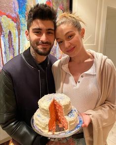 a man and woman standing next to each other holding a cake