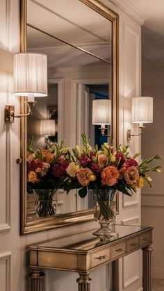 two vases filled with flowers sitting on top of a table next to a mirror