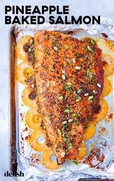 a piece of baked salmon with pineapple slices and seasoning on top in an aluminum pan