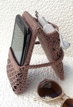 a crocheted cell phone case sitting next to a pair of sunglasses