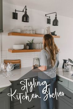 a woman standing at the kitchen counter holding a wine glass and looking into the sink